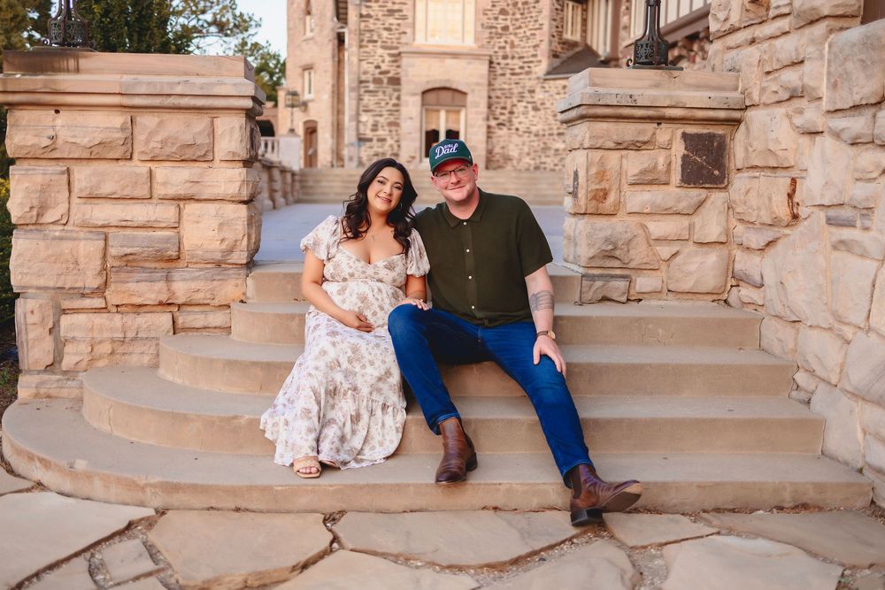 A pregnant woman and a man sit together on stone steps during an outdoor photo session at a rustic location.  HIghlands Ranch mansion