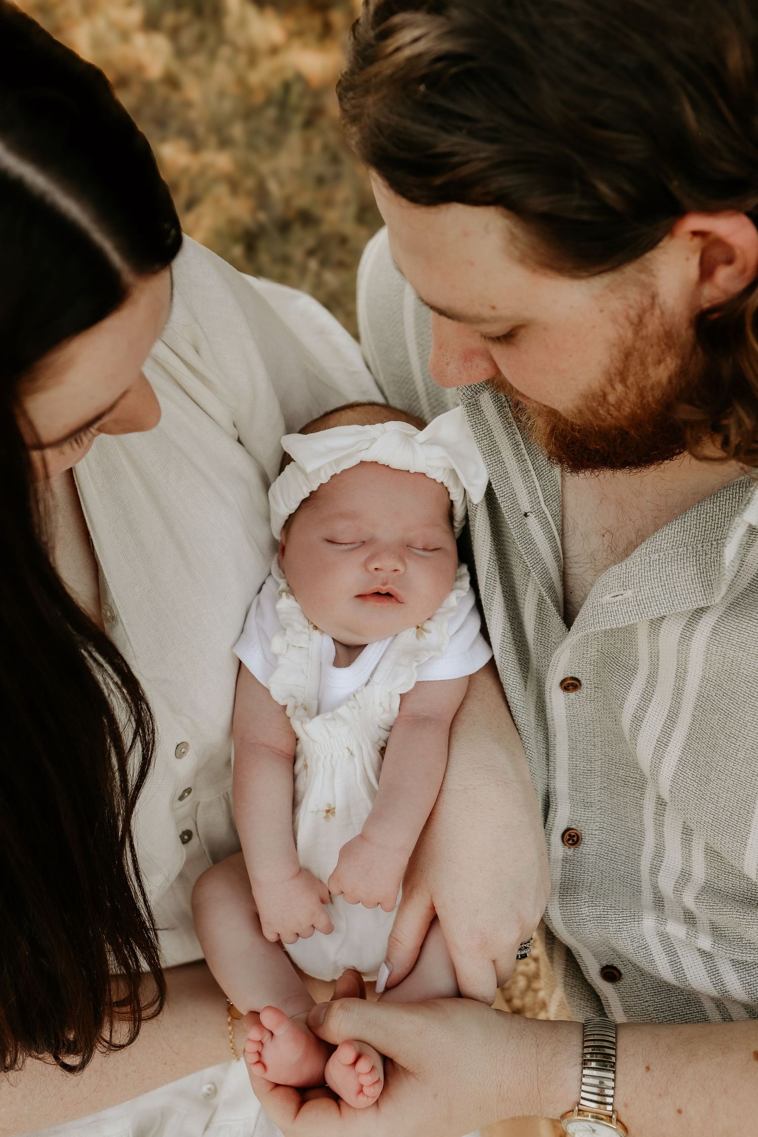 A series of intimate newborn photography shots showing parents holding a baby in white clothing against a neutral background.