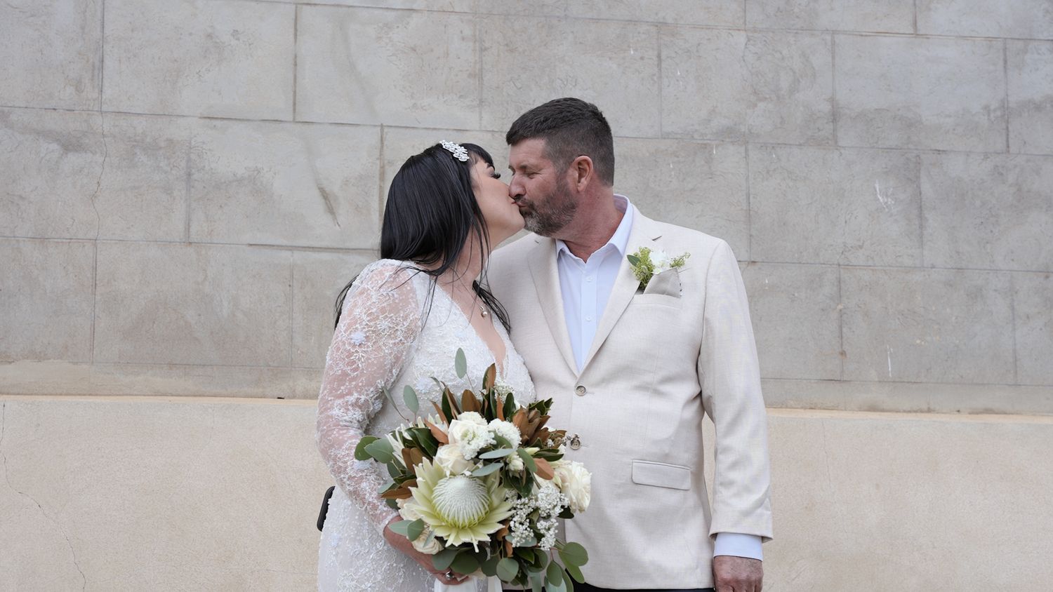 Elegant couple sharing an intimate moment against a stone wall backdrop.