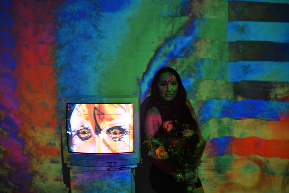 NikitaVisiion, founder of MHYSA Consultancy holding flowers in front of her immersive visual art projected  on art gallery walls