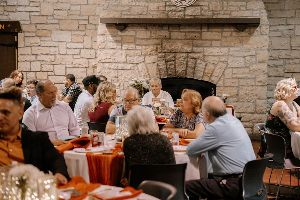 Diners seated at long wooden tables in a rustic brick-walled restaurant space enjoying a communal meal.