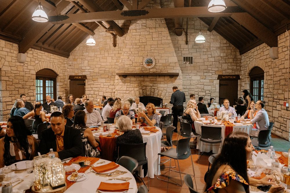Wedding reception guests mingle and dine in an elegant rustic venue with exposed brick walls and wooden beams.