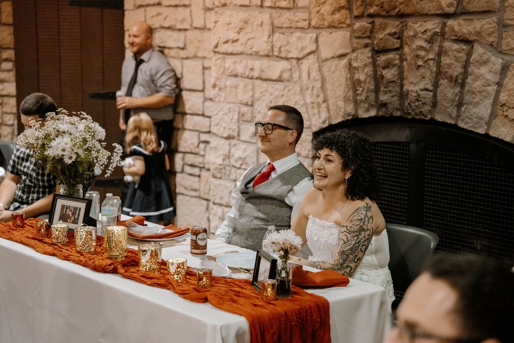 Wedding reception guests gather at tables in a rustic stone-walled venue with warm lighting and festive decorations.