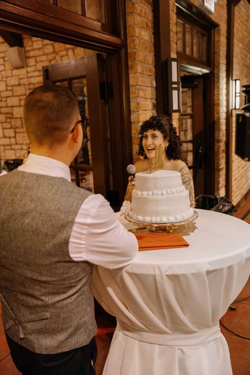 A couple sits together at their wedding reception in a rustic brick venue with white tablecloths.