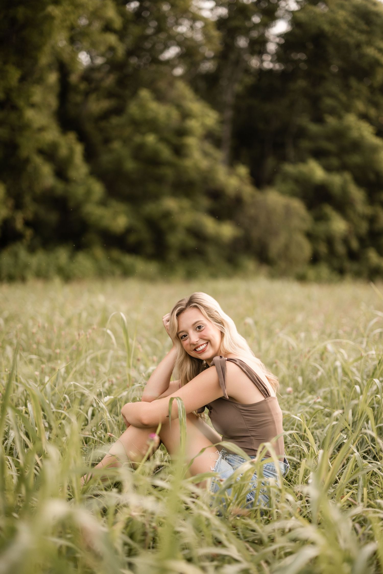 A joyful woman in casual attire lies in a grassy meadow on a sunny day, showing genuine happiness and relaxation.