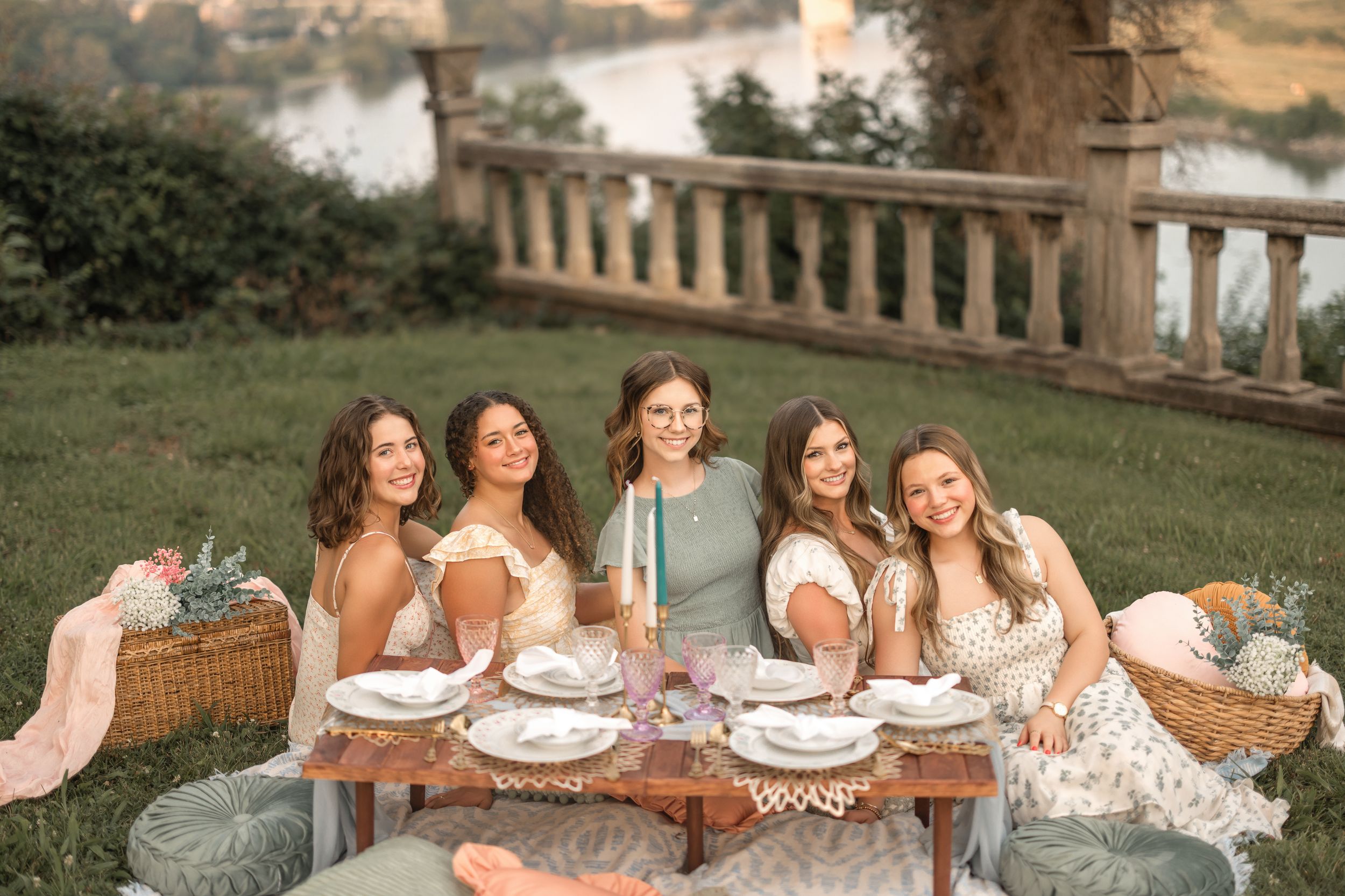 A group in matching floral dresses sits together at an outdoor dining table during a sunny afternoon celebration.