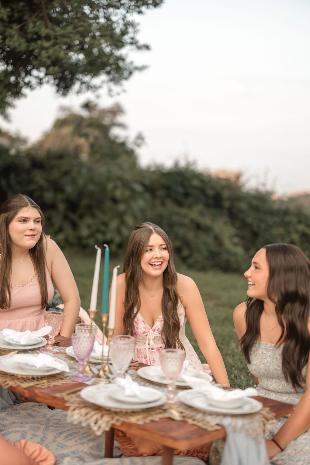 A group gathered around a rustic wooden table for an outdoor meal in natural lighting.