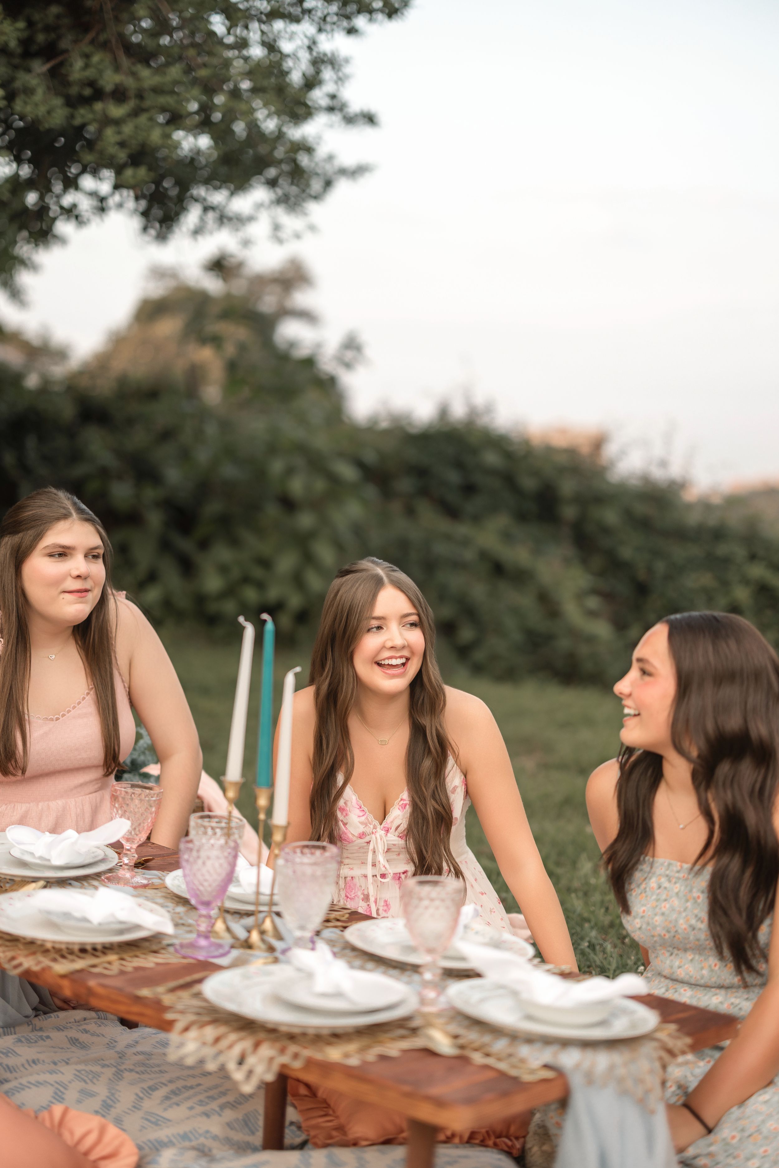 A group gathered around a rustic wooden table for an outdoor meal in natural lighting.