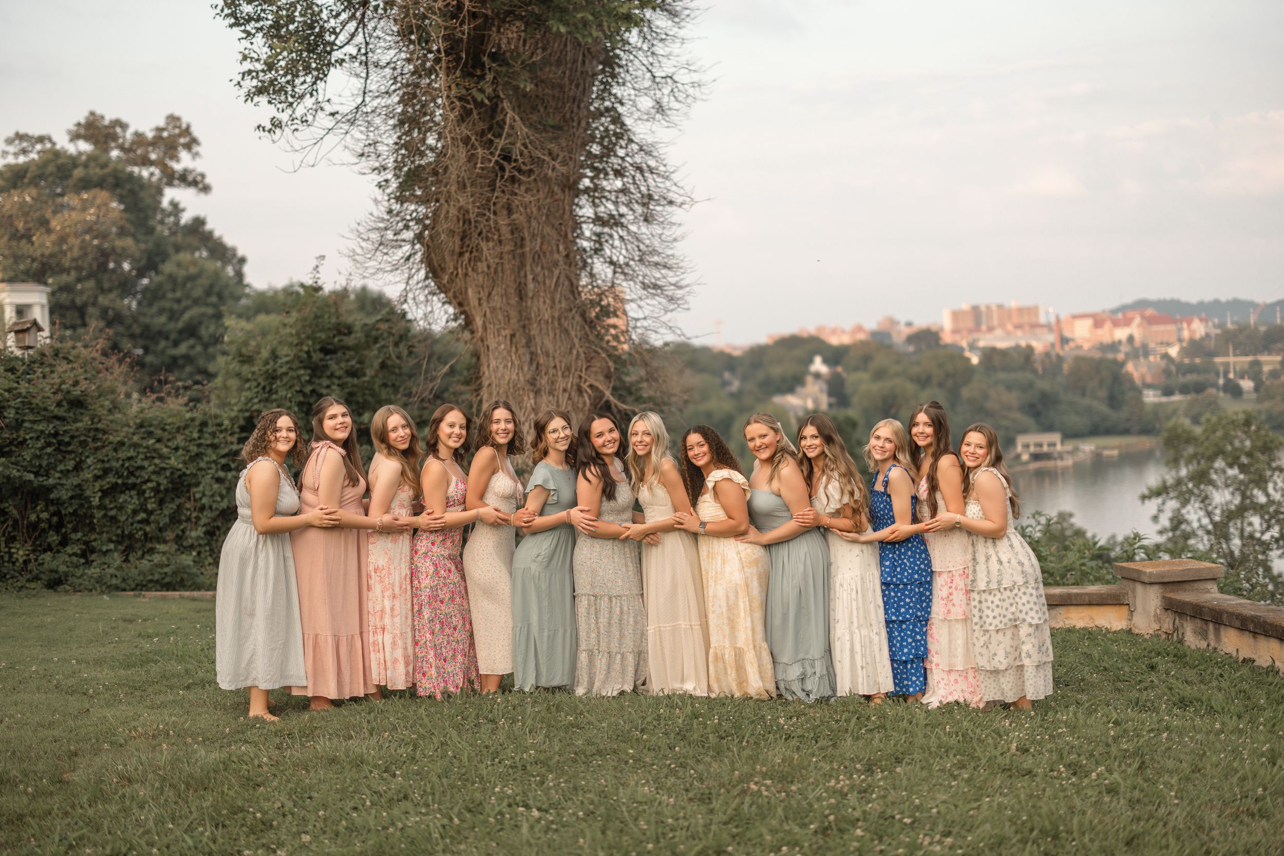 A group of people wearing pastel bridesmaid dresses pose together outdoors during golden hour.