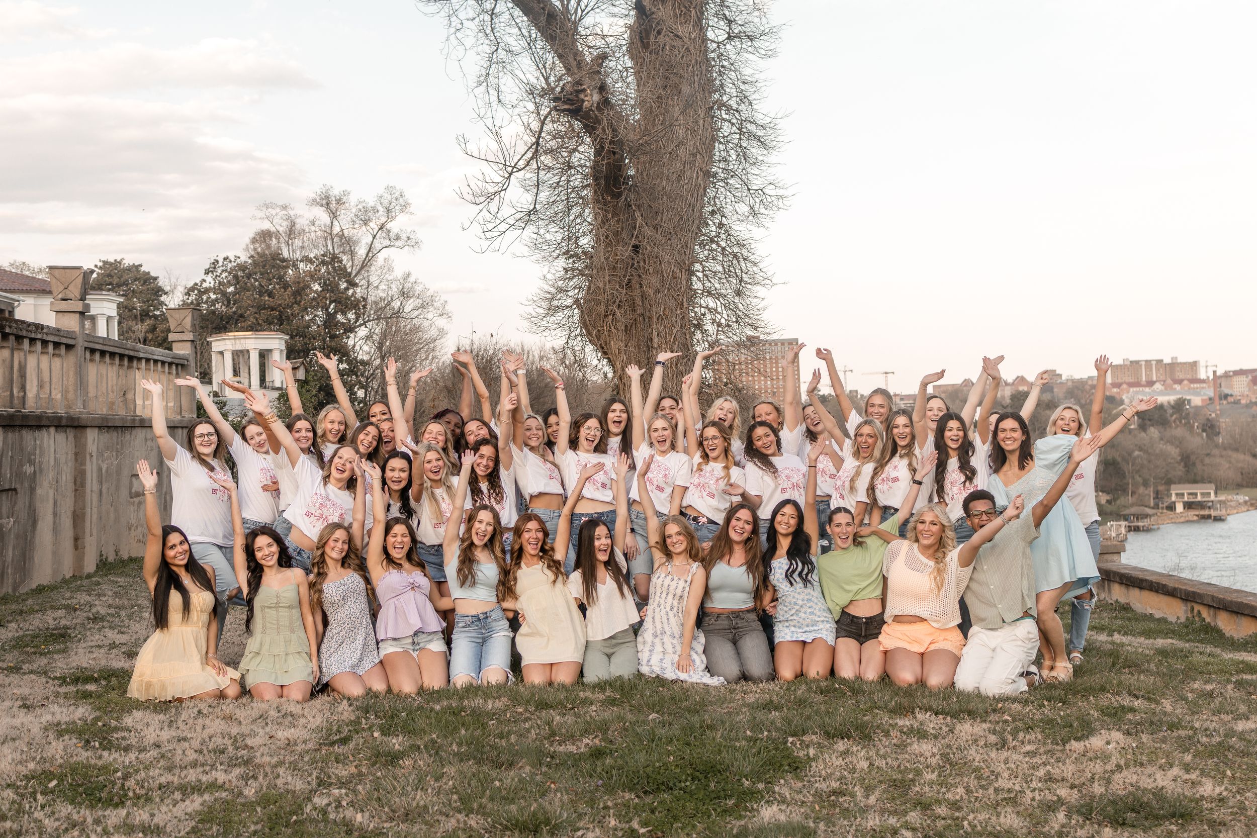 A group of people in light colored dresses pose together outdoors during a celebratory gathering.