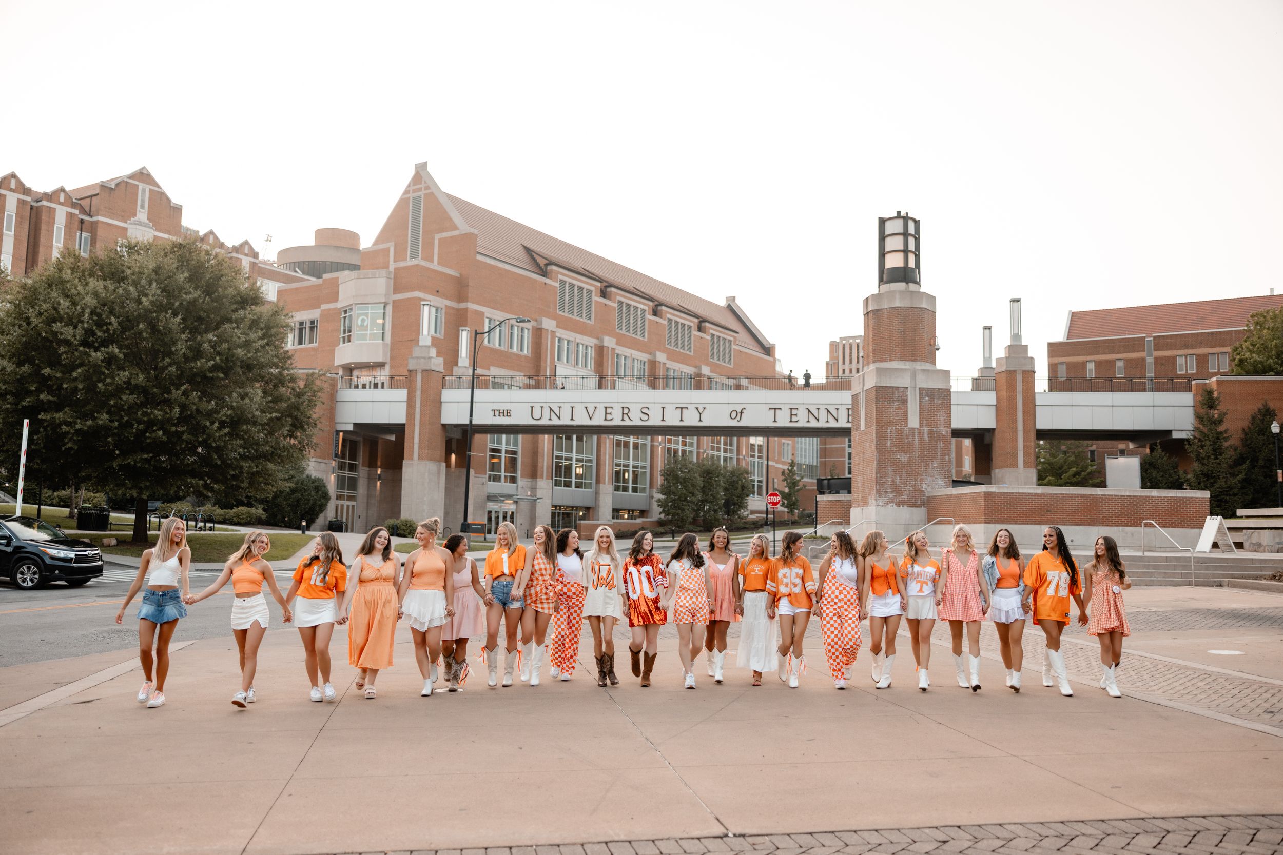 Wedding party walking in a line wearing orange and white dresses across a brick courtyard.