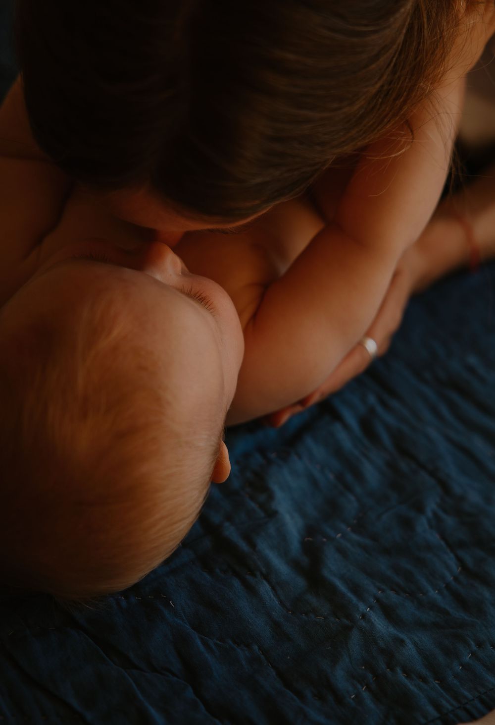 Close-up portrait showing tender interaction between parent and baby against blue textured background.