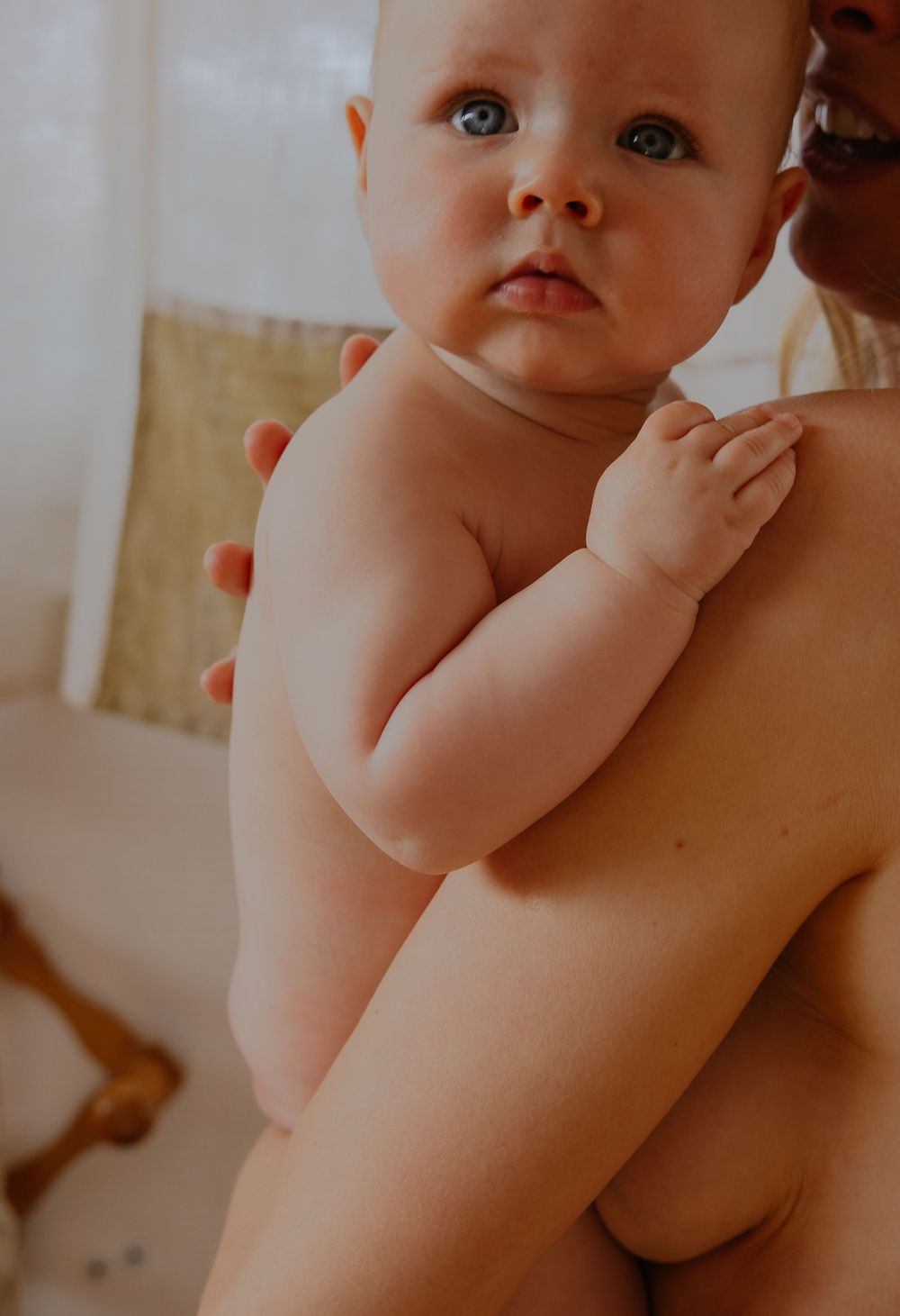 A baby with bright blue eyes gazes upward while being held during bath time.