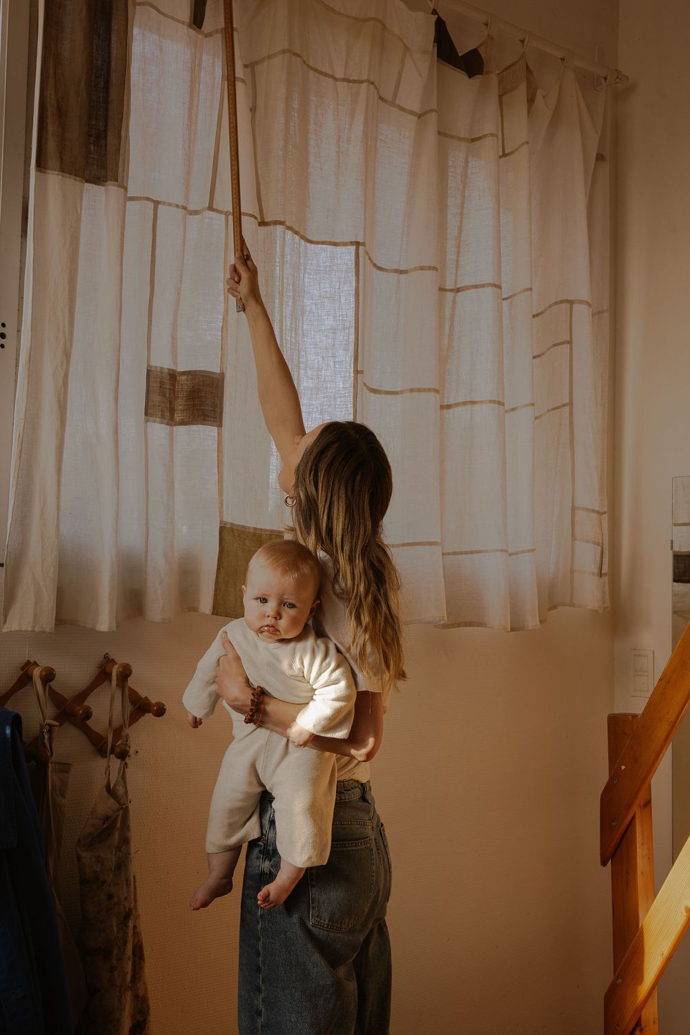 A parent and child dance together in front of white curtains in a sunlit room, creating playful shadows.