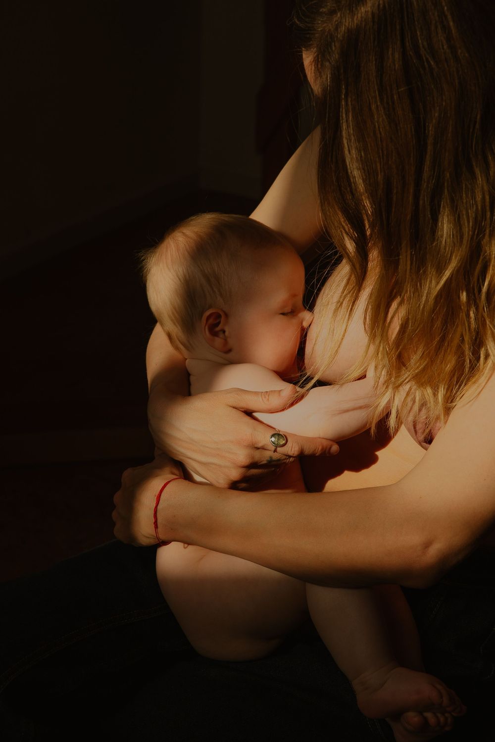 Intimate moment of mother breastfeeding infant in dark moody lighting with warm tones.