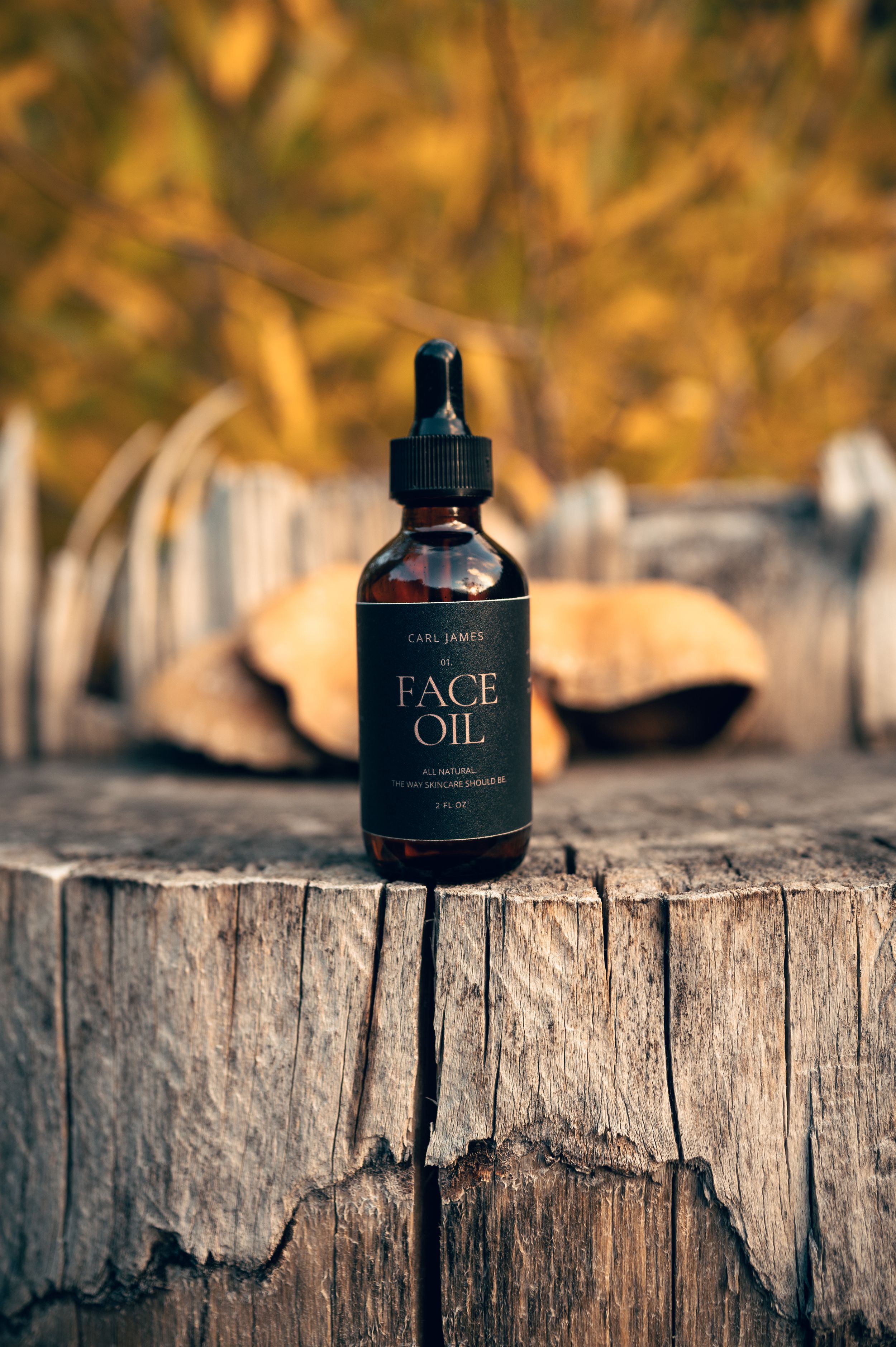 Carl James all-natural face oil in amber dropper bottle on rustic wood stump with autumn foliage background.