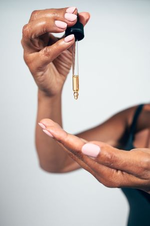Close-up of hand holding dropper applicator dispensing golden face oil serum over palm.
