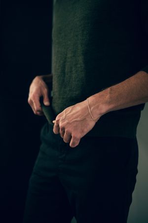 Close-up of man's hands wearing a delicate chain bracelet against dark background with green shirt.
