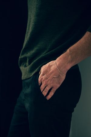 Close-up of man's hand with minimalist chain bracelet resting at side wearing dark green sweater.