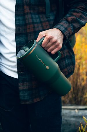 Man in plaid flannel shirt holding a large forest green HydroJug tumbler with gold accents outdoors.