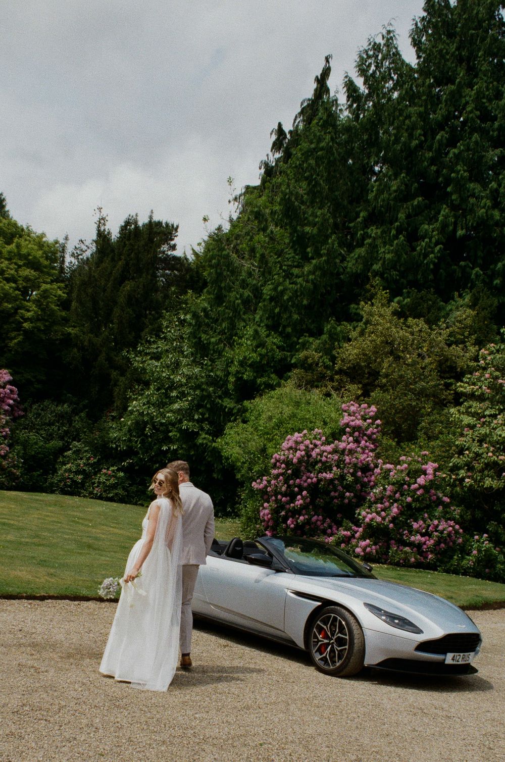 A sequence of wedding photos showing a bride walking past a silver sports car with pink rhododendrons in the background.