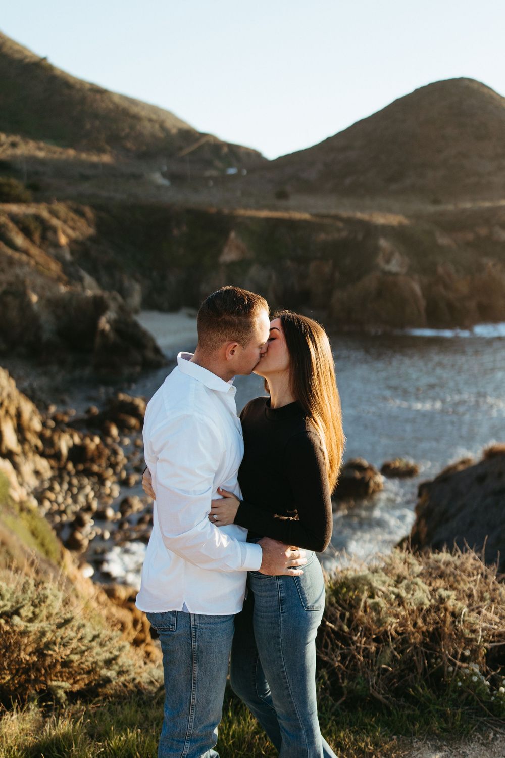 Couple sharing intimate moments along a scenic coastal cliff during golden hour.