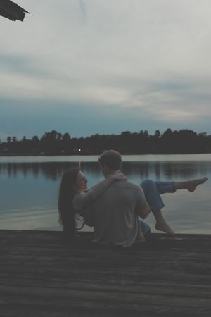 Couple relaxing on a dock during sunset over a serene lake.