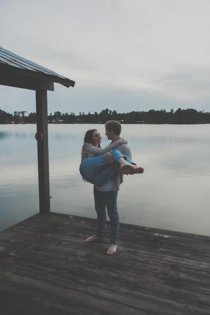 Romantic moment shared between two people on a lakeside dock at dusk.