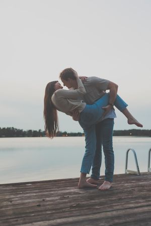 Couple performing romantic dance moves on a wooden dock overlooking a serene lake.