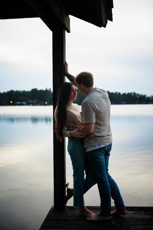 Silhouetted figures sharing an intimate moment on a dock overlooking a serene lake at sunset.