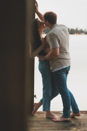 Two people embracing on a wooden dock with a misty lake view in the background.