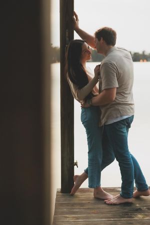 A couple shares an intimate moment on a wooden dock by the water.
