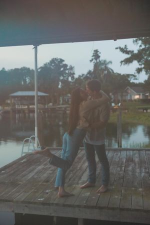 Two people sit together on a wooden dock overlooking a serene lake at dusk.