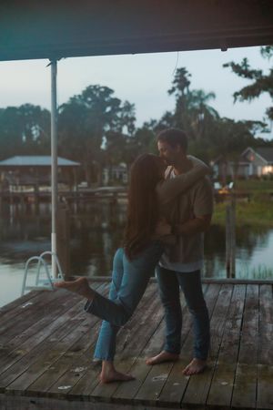 Romantic couple sharing intimate moments on a wooden dock by the water at sunset.