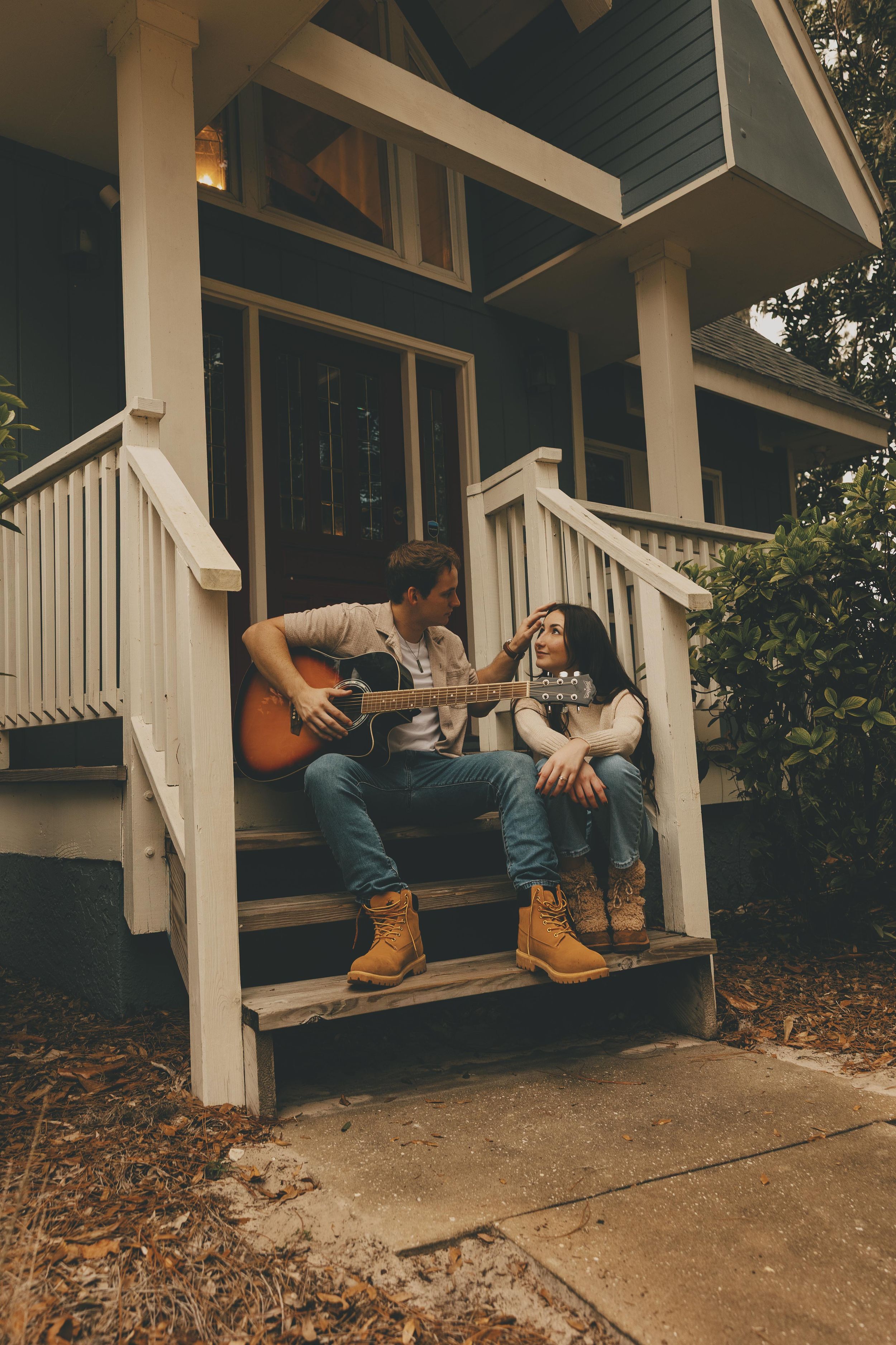 Couple relaxing on a rustic front porch of a house with white columns and fallen leaves.