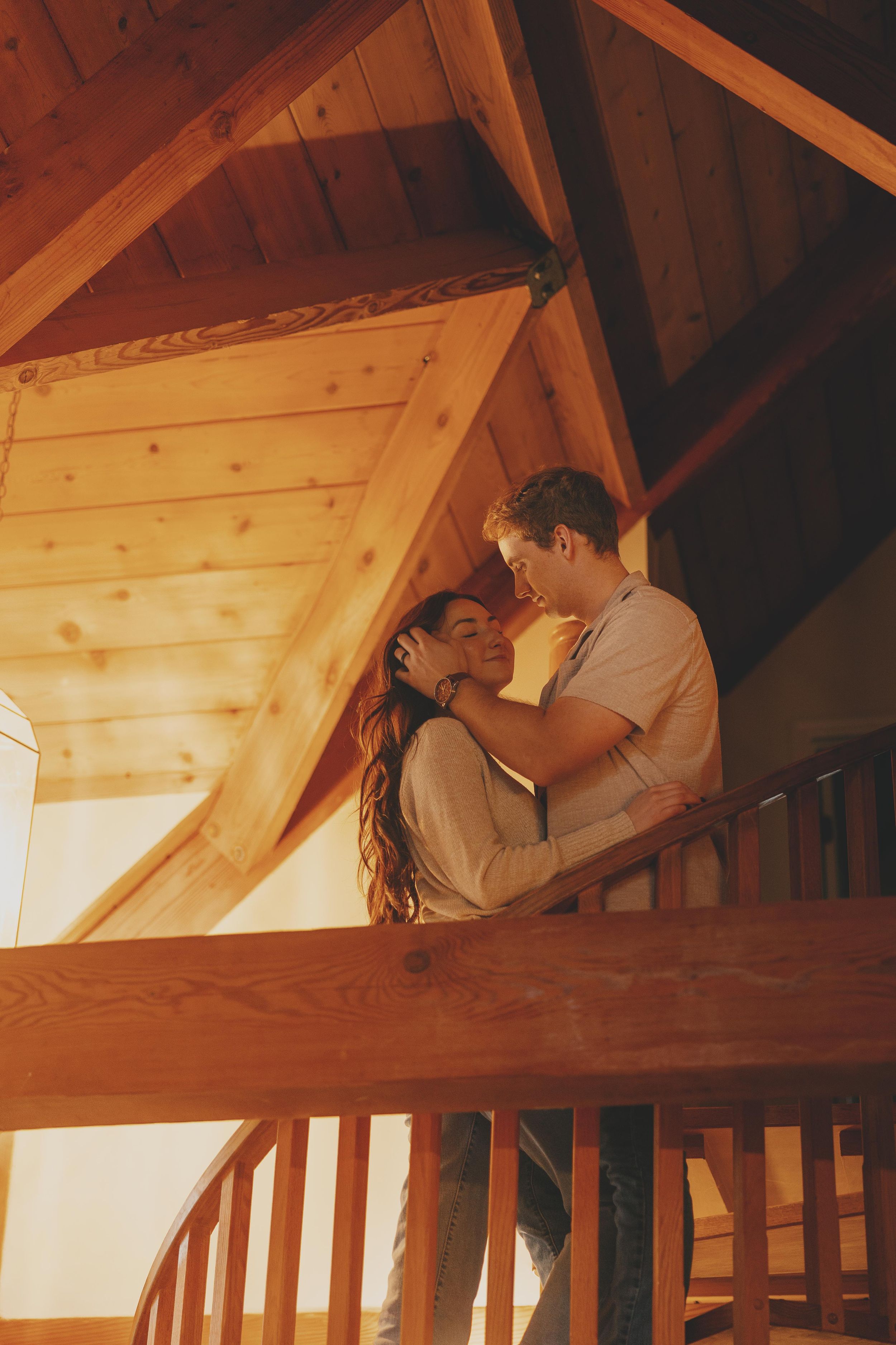 A romantic couple shares an intimate moment in a cozy wooden loft with warm lighting.