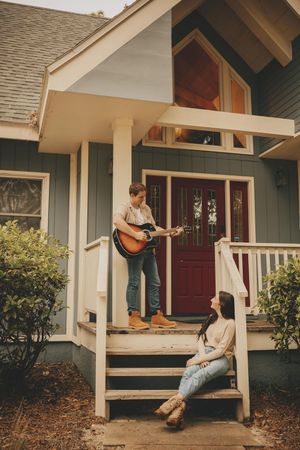 Couple relaxing on a front porch with an acoustic guitar on a sunny afternoon.