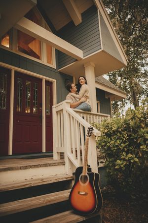Acoustic guitar leaning against white porch railing of craftsman style house at sunset.