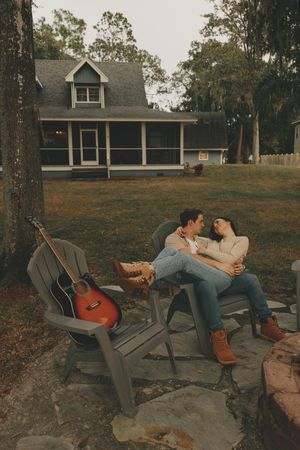 Friends lounging on outdoor chairs at dusk with a view of a house on a hill.