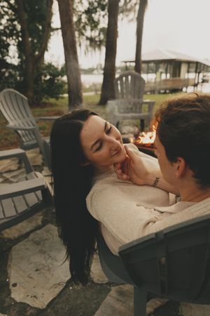 Couple sharing a romantic moment in wooden Adirondack chairs at sunset.