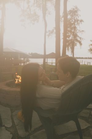 People relax on outdoor lounge chairs at sunset with a fire pit glowing in the background.