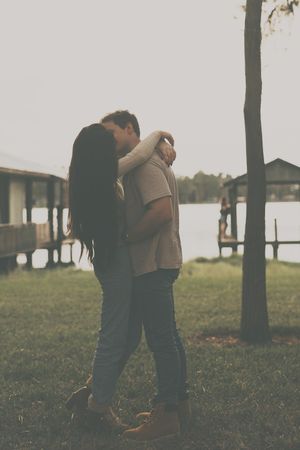 Couple embracing in a scenic outdoor setting with trees and water in the background.