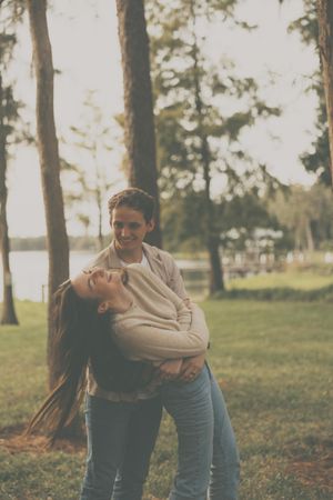People enjoying a playful moment together in a grassy field with tall pine trees in the background.