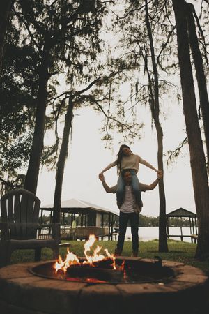 People celebrating around a bonfire with trees and water in the background at sunset.