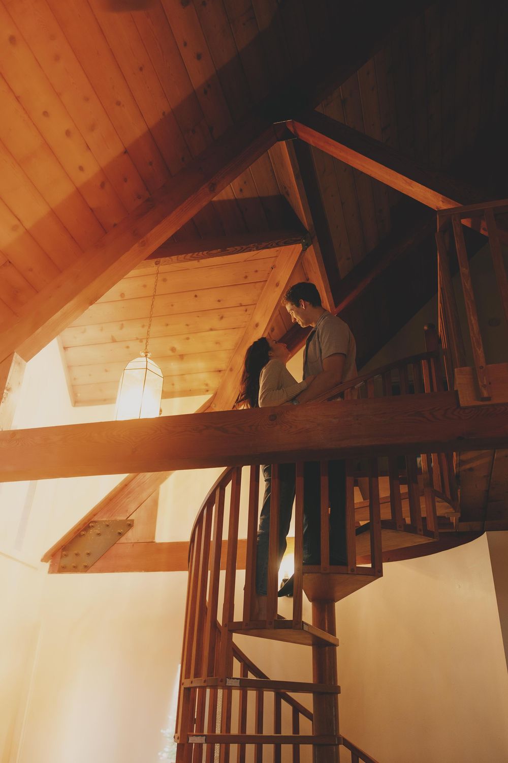 Wooden beams and rafters create geometric patterns in a warm-lit attic space with rustic architectural details.
