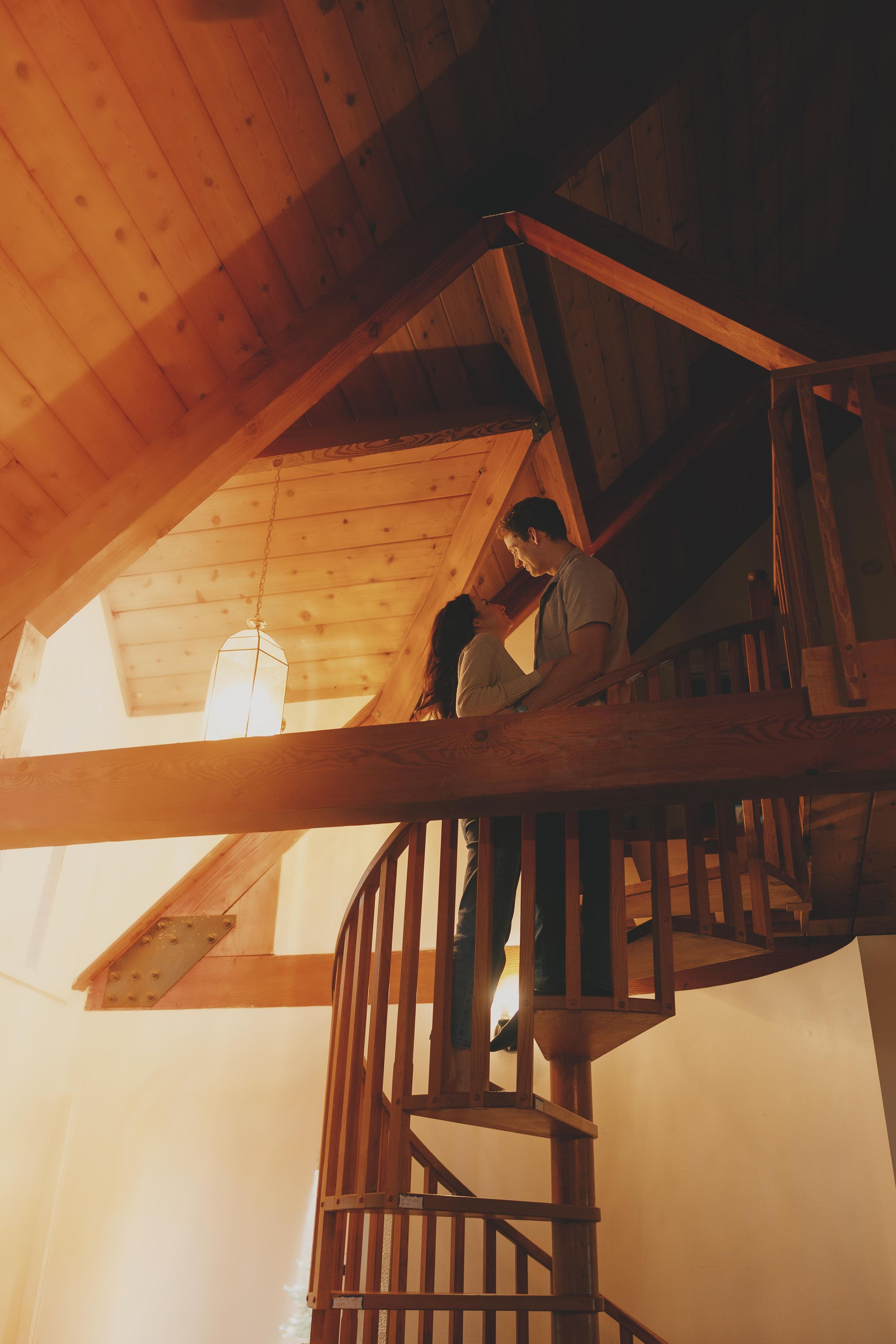 Wooden beams and rafters create geometric patterns in a warm-lit attic space with rustic architectural details.
