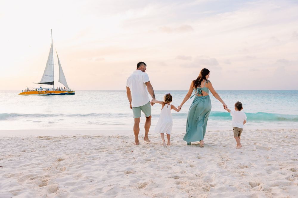 Family walking together on white sandy beach with sailboat visible in turquoise waters.