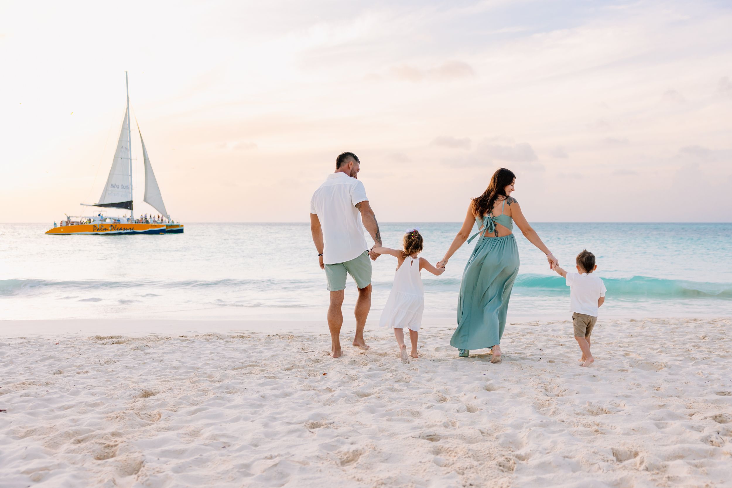 Family walking together on white sandy beach with sailboat visible in turquoise waters.