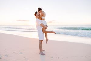 Romantic beach photoshoot with couple embracing on sandy shore during golden hour.