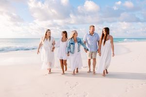 Family group dressed in white and blue walking together on tropical beach.